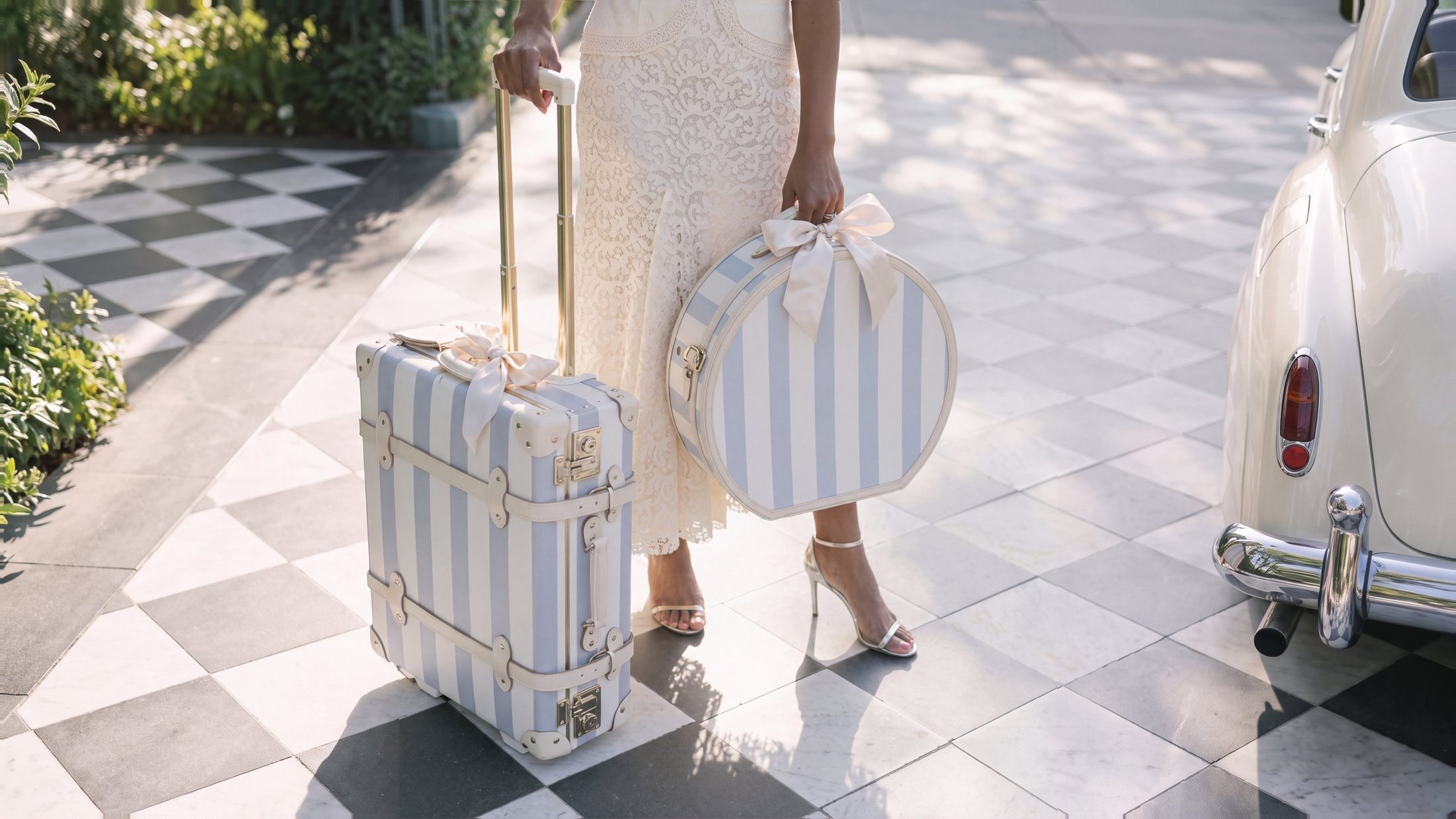 Blue and ivory striped luggage with satin bows beside a vintage car on a checkered marble driveway