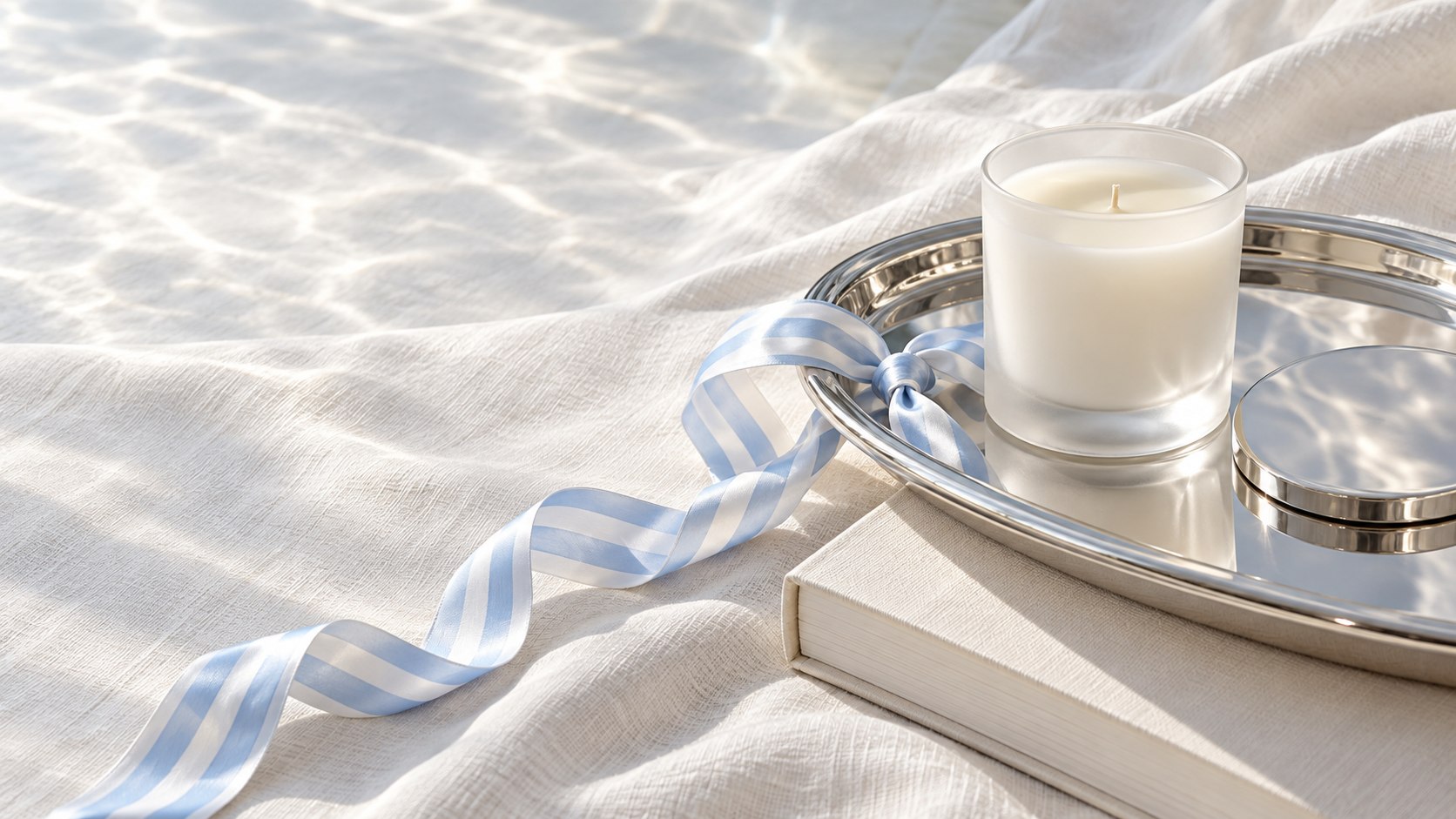 A white candle on a silver tray with a striped ribbon on ivory linen