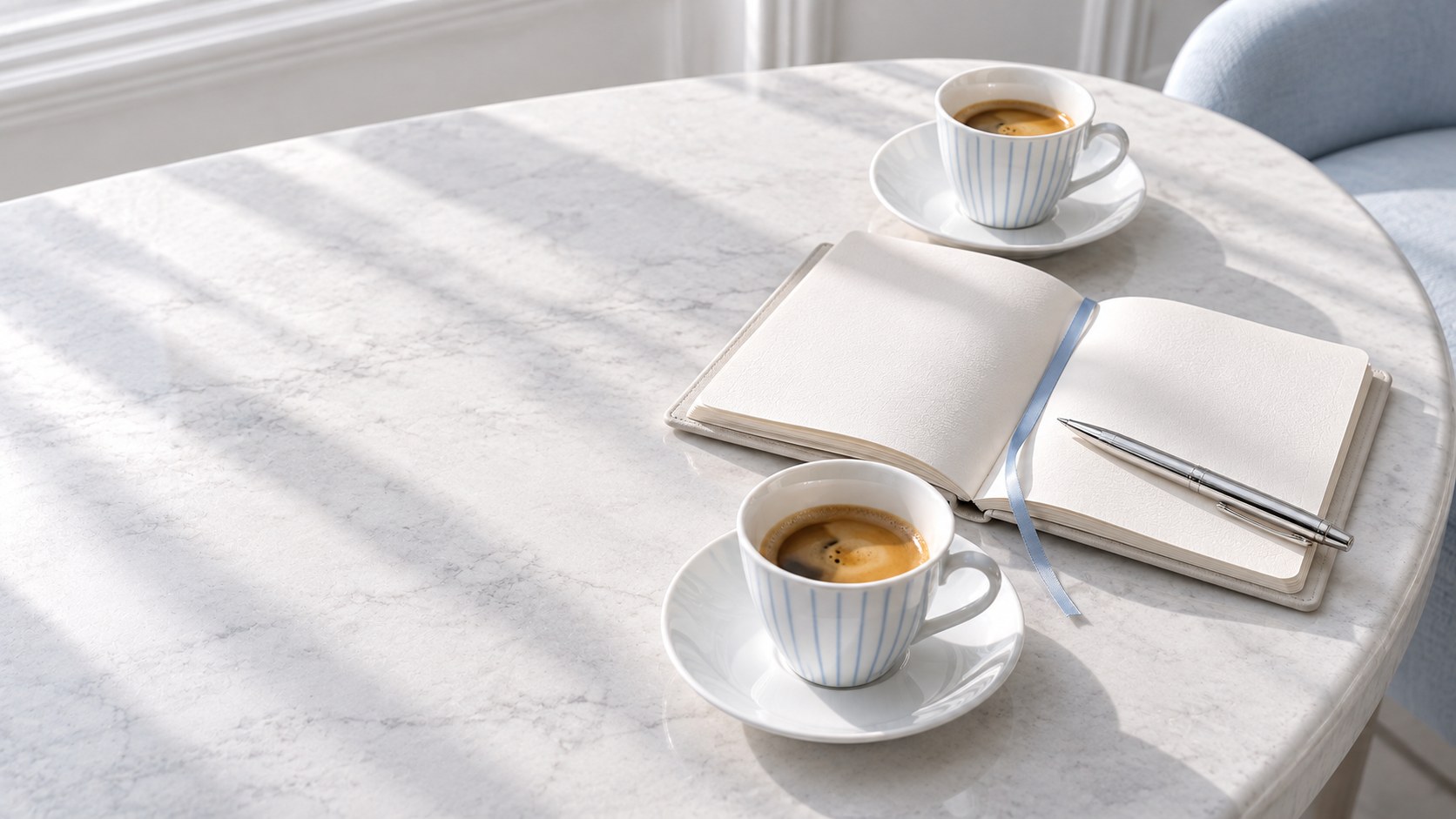 Two striped espresso cups and an open notebook with a silver pen on a marble table